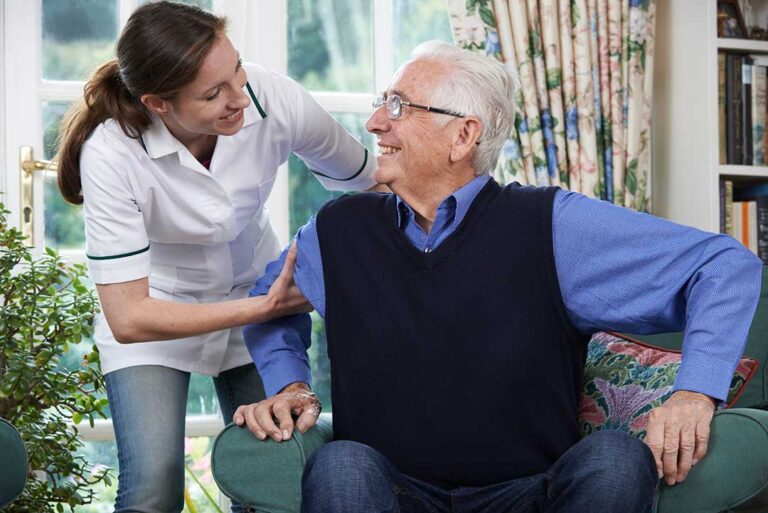 Senior residents enjoying time together in a bright, plant-filled common area with natural sunlight and energy-efficient lighting.